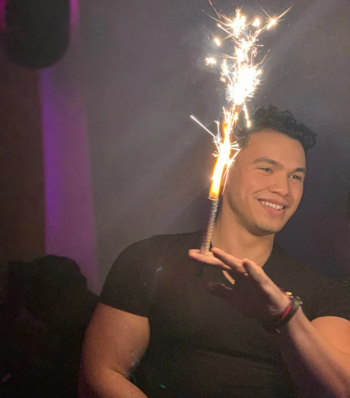 John smiling under purple club lights, holding a lit sparkler
